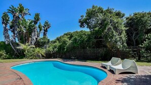 Una piscina de borde curvo, rodeada por un sendero de ladrillo y una valla de madera.