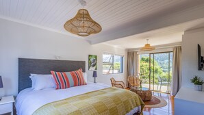 Un dormitorio con una cama grande, una ventana con vistas a la vegetación, muebles de mimbre y un techo con vigas de madera.