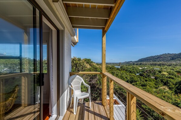 A balcony with a wooden railing, a white plastic chair, and a view of a lush green landscape.