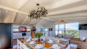 Una cocina moderna con armarios blancos, salpicadero rojo y un comedor con una mesa de madera preparada para seis comensales.