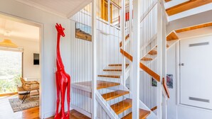 Un interior moderno con una escalera de caracol, una escultura de una jirafa roja y vistas de vegetación al exterior.