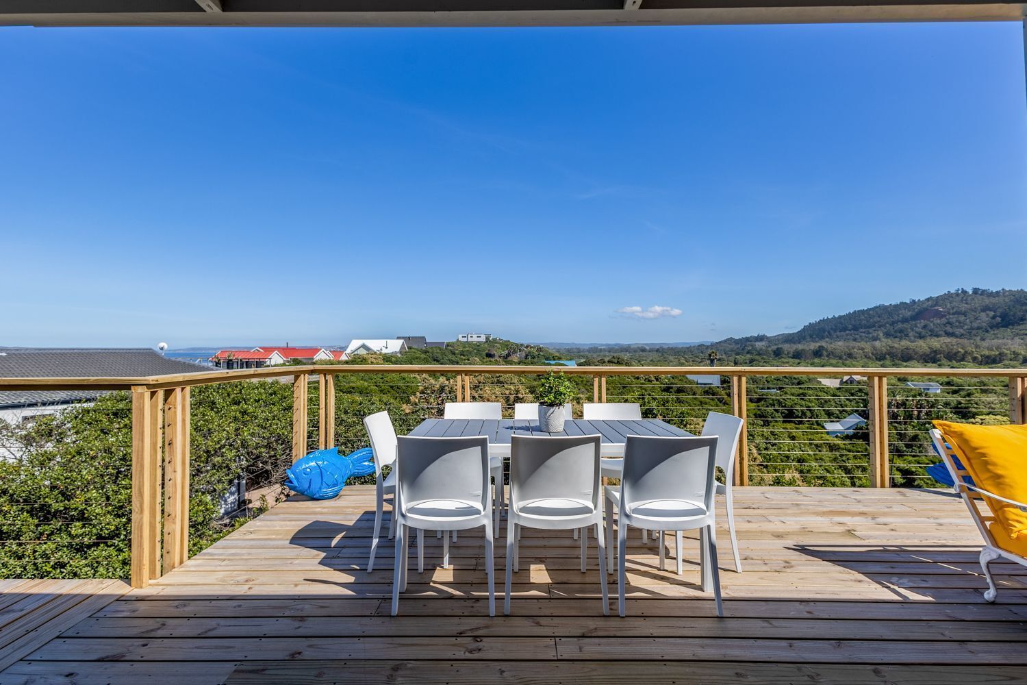A wooden deck with a table and chairs, overlooking a vineyard and distant buildings.