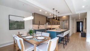A modern kitchen with a central island, pendant lighting, and a dining area with a wooden table and white chairs.