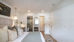 A bedroom with a bed, bedside lamps, a headboard, and a view into the bathroom.