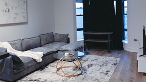Una sala de estar moderna con un sofá seccional gris, una mesa de centro con estructura de metal y una alfombra estampada.
