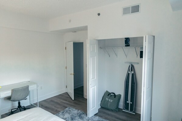 Un dormitorio con cama, escritorio, silla, armario y bolso.