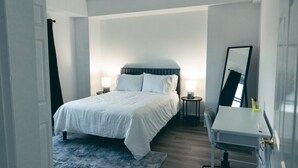 Una habitación de hotel con cama, mesitas de noche, escritorio y espejo.