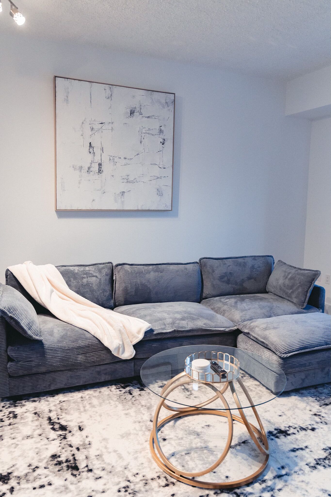 A modern living room with a grey sectional sofa, a round coffee table with a metal base, and a large abstract painting on the wall.