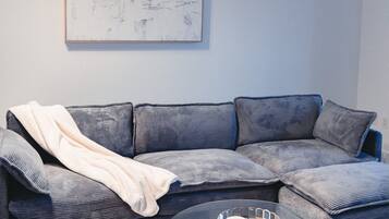 A modern living room with a grey sectional sofa, a round coffee table with a metal base, and a large abstract painting on the wall.