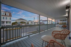 Una terraza techada al aire libre con mobiliario de mimbre, barandilla y vistas a casas.