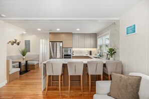 Una cocina moderna con una isla central, taburetes de bar y un área de comedor con un sofá blanco.