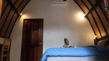 A bedroom with a sloped ceiling, a wooden door, a bed with a blue cover, and a wall-mounted air conditioning unit.