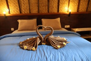 Un lit avec une couvre-lit bleue, deux oreillers et une serviette pliée en forme de cygne, agrémentée de fleurs.