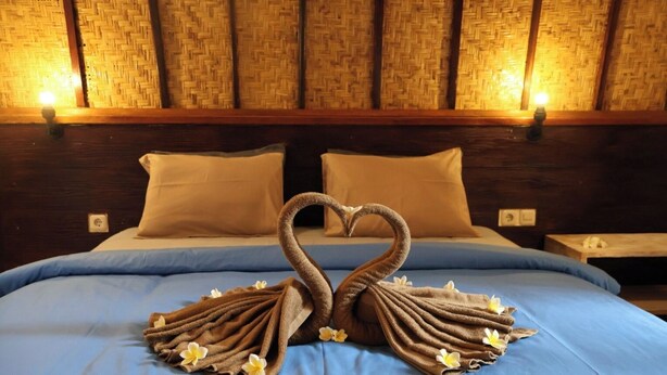 A bed with a blue bedspread and two pillows, a woven headboard, and a nightstand with a lamp.