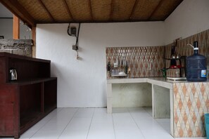 Une cuisine avec un sol carrelé, une étagère en bois, une cuisinière à gaz et un distributeur d’eau.