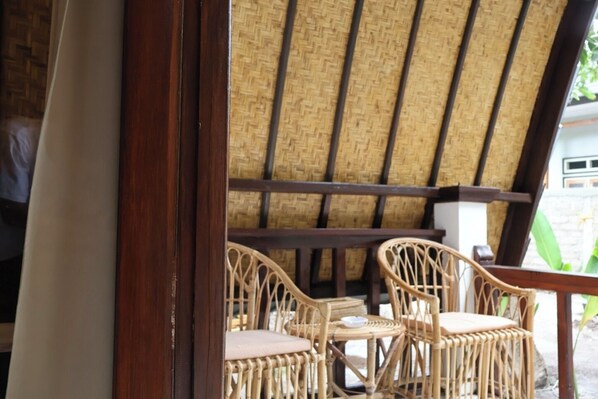 A covered outdoor seating area with wicker chairs and a table, featuring a thatched roof and wooden beams.