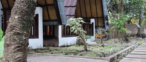 A traditional house with a thatched roof, a wooden fence, and a bicycle parked outside.