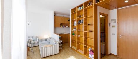 A spacious room with a large wooden bookshelf, a striped sofa, and a kitchen area.