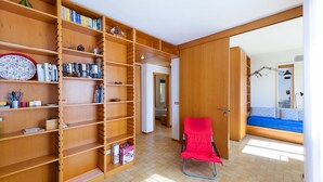 A room with a wooden bookshelf, a red chair, and a bed with a blue bedspread. - CASA LUISA A CAPO'DARCO - CASA LUISA (Rio Marina)