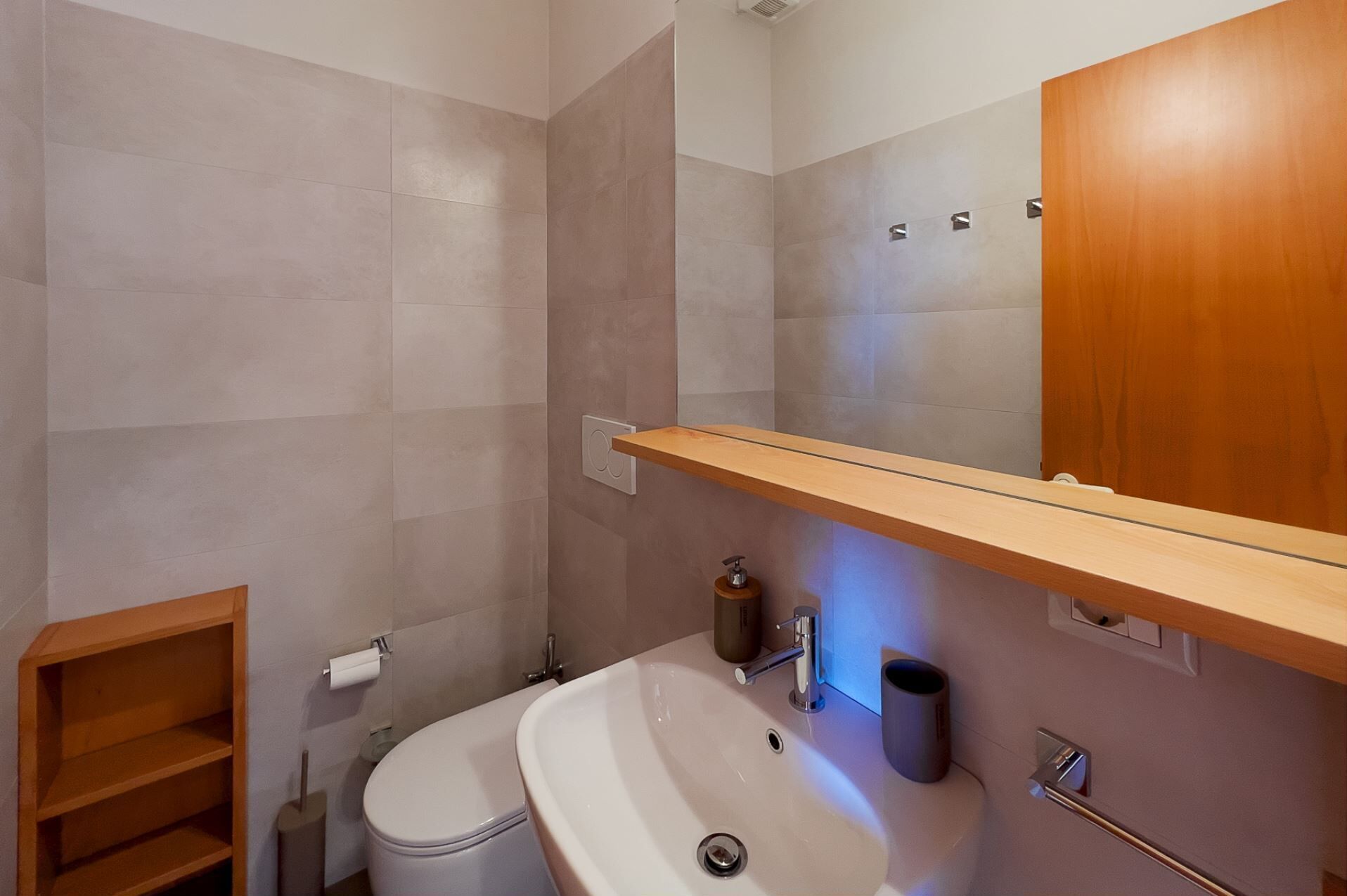 Ein Badezimmer mit einem weißen Waschbecken, einer Toilette und einem Holzregal darüber.