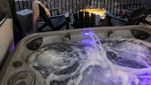Un jacuzzi con cascada, rodeado por una terraza de madera y mobiliario exterior.