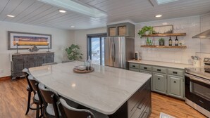 A modern kitchen with a large island, stainless steel appliances, and a view through the door. - Calamity Jane’s Hidden Haven – 12.5 private acres, multiple patios, fire pit & 4 king suites! (Lead)