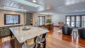 A spacious kitchen with a large island, wooden flooring, and large windows offering views of trees. - Calamity Jane’s Hidden Haven – 12.5 private acres, multiple patios, fire pit & 4 king suites! (Lead)