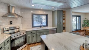 A modern kitchen with a large island, built-in oven, and a skylight. - Calamity Jane’s Hidden Haven – 12.5 private acres, multiple patios, fire pit & 4 king suites! (Lead)