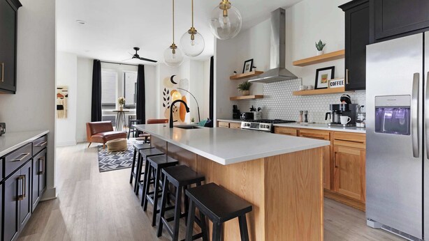 A modern kitchen with a central island, bar stools, a stainless steel refrigerator, and pendant lighting.