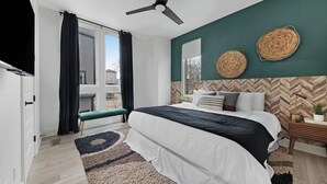 A modern bedroom with a bed, a bench, a ceiling fan, and a view of the outside.