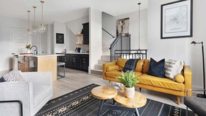 A modern living room with a sofa, coffee table, and a staircase leading to an upper level. - The Bluestem - Stylish Design, Rooftop w/ Firepit! (Nashville)