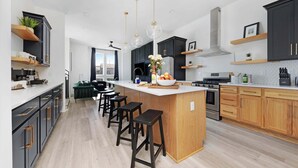 A modern kitchen with a central island, bar stools, and pendant lighting.