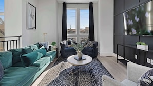 A modern living room with a green sofa, a round coffee table, and a TV on the wall.