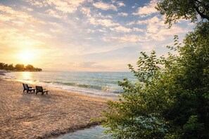 Una playa con dos sillas de madera y una mesa, una orilla arenosa, y vistas al mar y al cielo.