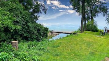 A grassy area with a small wooden bridge over a body of water, a bicycle, and a small white structure.