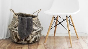 A white chair with wooden legs and a woven basket with a gray cloth on the floor.