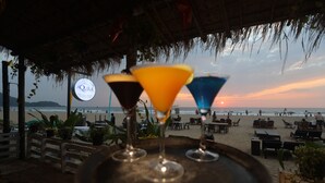 A beachside bar with a thatched roof, a sign reading "AQUILA," and three colorful martini glasses on a tray. - Aquila Boutique Resort Agonda (Canacona)