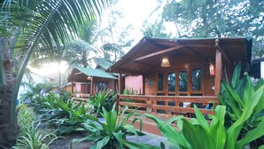 Une cabane en bois dotée d’une véranda, entourée d’une végétation tropicale luxuriante.