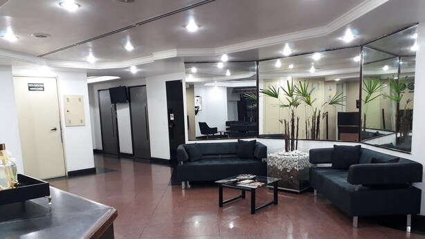 Eine moderne Lobby mit einer Rezeption, dunklen Sofas, einem Couchtisch und einem großen Spiegel, der den Raum reflektiert.