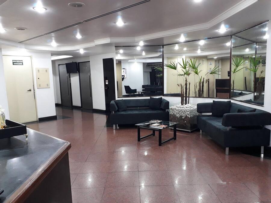 A modern lobby with a reception desk, dark sofas, a coffee table, and a large mirror reflecting the space.