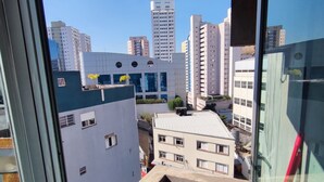 Blick von einem Balkon auf eine Stadtlandschaft mit modernen Gebäuden, darunter ein weißes Gebäude mit blauem Dach und ein höherer, weißer Bau mit markanter Architektur.