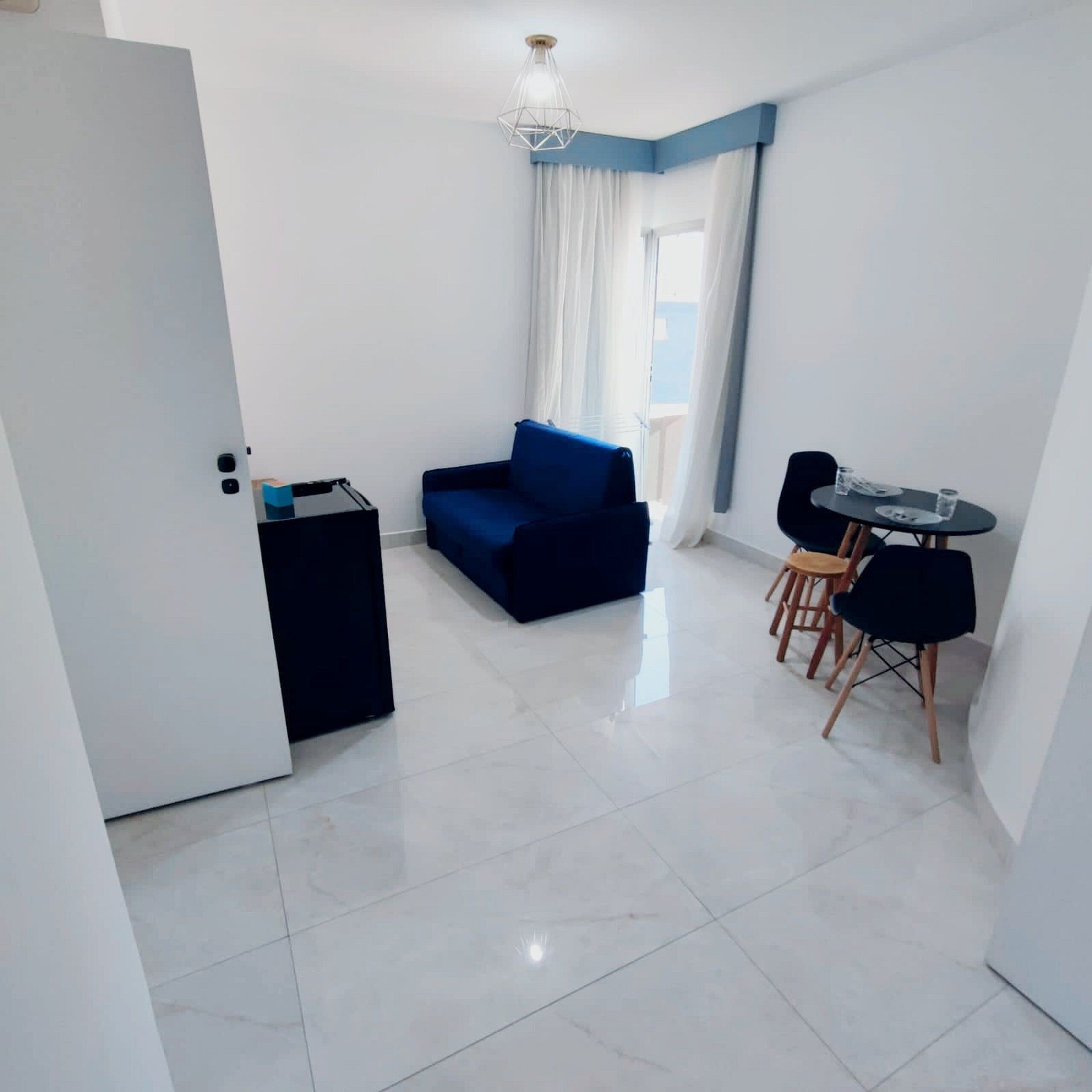 A modern living room with a blue sofa, a small black side table, and a dining area with a table and chairs.