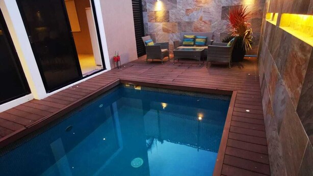A swimming pool with a wooden deck, a stone wall, and a seating area with cushions. - Charming 3-bedroom house with Private Pool in lovely Cancun (Cancun)