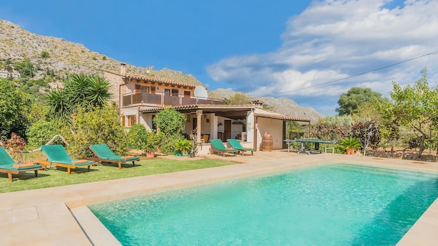 A poolside view of a Mediterranean-style villa with a swimming pool, green lounge chairs, and a mountainous backdrop. - Can Ventet by SunVillas Mallorca (Pollença)