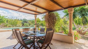 A covered outdoor dining area with a pool view, stone flooring, and lush greenery. - Can Ventet by SunVillas Mallorca (Pollença)