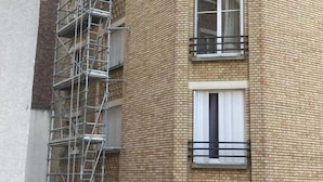 Un immeuble à plusieurs étages, doté d’une façade en briques, de nombreux balcons et d’une structure d’échafaudage métallique sur le côté gauche.