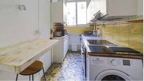 Une cuisine compacte équipée d’un lave-linge, d’une petite table et d’un sol carrelé.