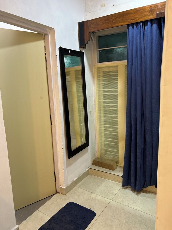 A small, enclosed room with a door, a window with a mesh screen, and a blue curtain.