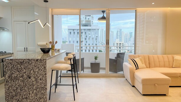 Cocina moderna con encimera de granito, taburetes de bar y vistas a la ciudad a través de amplios ventanales correderas.