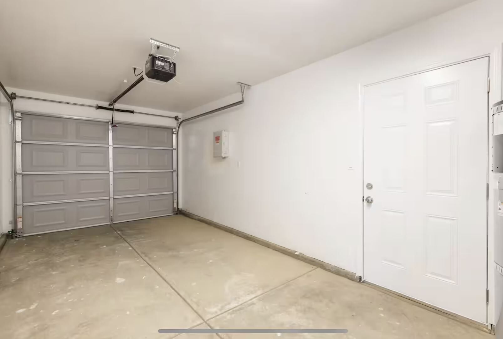 A clean, empty garage with a closed garage door, a white door, and a ceiling-mounted projector.